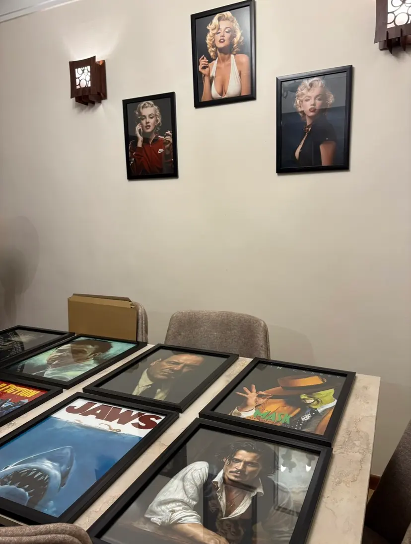 Framed Marilyn Monroe posters on a wall above a table of finished framed orders